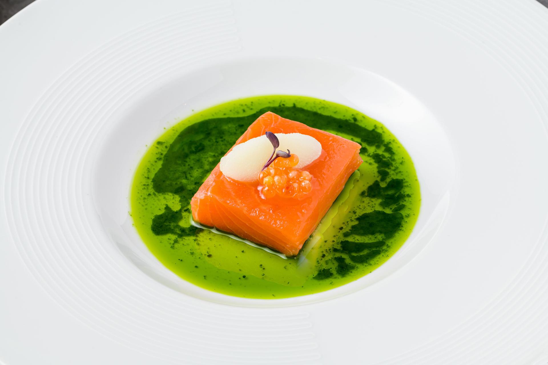 Sous-vide salmon fillet with fish roe, garnished with sorbet and microgreens, served on a vibrant green herb sauce